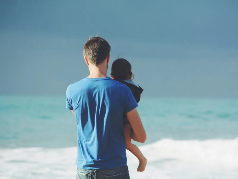 Dad on beach looking out to sea holding child