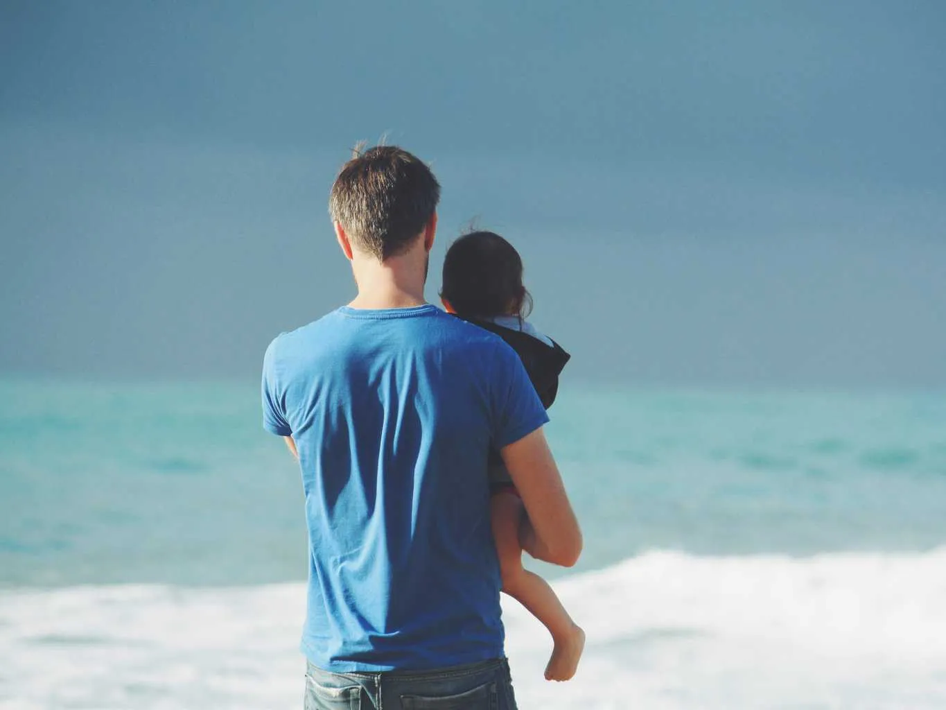 Dad on beach looking out to sea holding child
